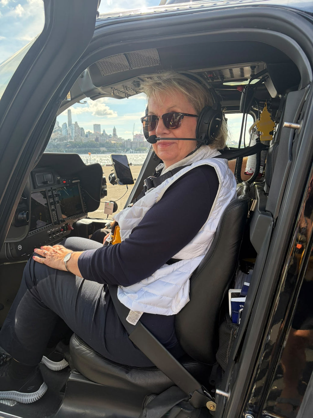 Moni in the cockpit of a helicopter wearing a headset in front of a skyline